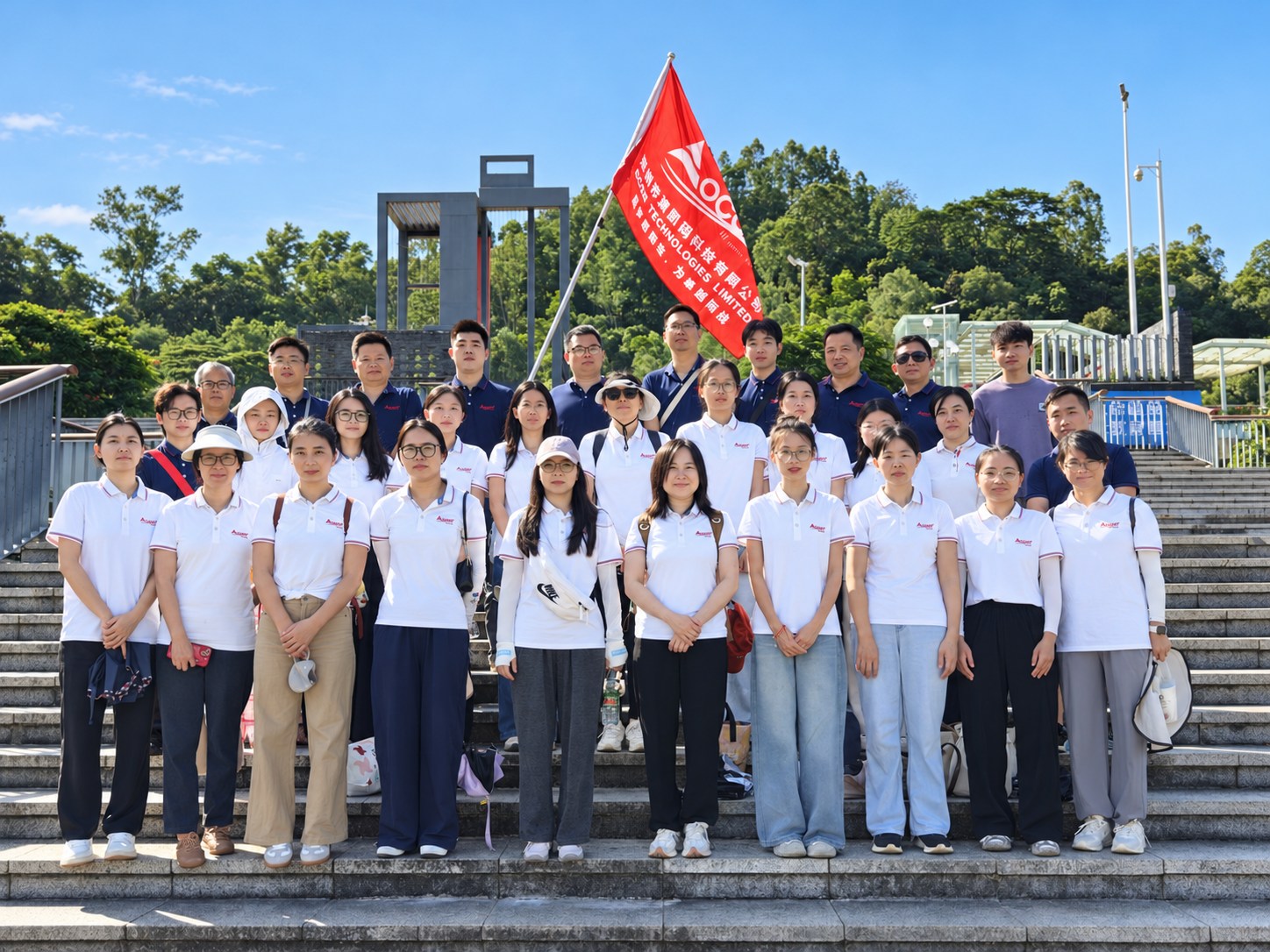 OCOM colleagues in company shirts pose together beneath the OCOM flag at Lixin Lake in Shenzhen.